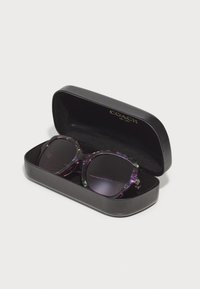 Lunettes de soleil dégradé violet dans un étui rigide noir. Les lunettes ont une monture épaisse à motif et des verres noirs avec des accents dorés.