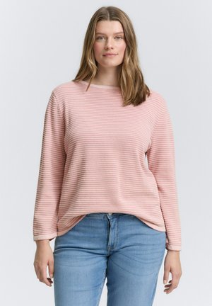 Un haut rose à manches longues avec une texture côtelée et des rayures horizontales, associé à un jean bleu clair. Le haut présente une coupe décontractée et ample.