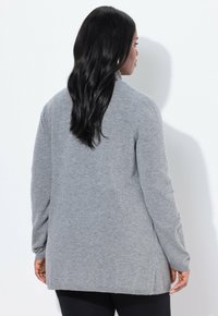 Grå långärmad cardigan med rak skärning, ribbade ärmslut, sidofickor och mjuk stickad struktur. Inga synliga detaljer eller mönster.