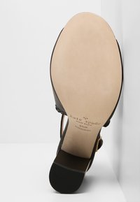 Černá kožená podešev s texturovaným povrchem, s hladkým světlým vnitřním stélkou a embosovaným logem značky. Elegantní design pásků je viditelný.