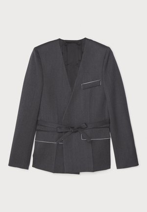 Graue Wickeljacke aus strukturiertem Stoff, mit langen Ärmeln, einem Gürtel in der Taille und einer einzelnen Brusttasche mit weißem Besatz.
