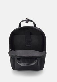 Sac à dos noir avec un extérieur lisse, fermeture éclair et un intérieur spacieux gris. Comprend une petite étiquette logo et une poignée supérieure pour le transport.