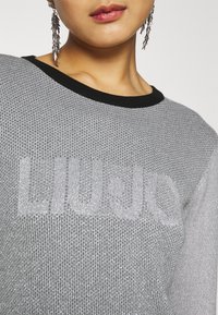 Silberner Strickpullover mit einem schwarzen gerippten Kragen, auf dem der Markenname "LIUJO" in leicht erhobener Textur zu sehen ist.
