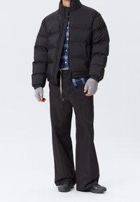 Chaqueta negra acolchada con un cuello alto, combinada con una camisa de cuadros y pantalones oscuros de corte holgado. Guantes grises sin dedos y zapatos negros.