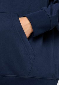 Felpa blu navy con finitura testurizzata, dotata di tasca a marsupio e polsini a costine. Il tessuto è morbido e leggermente elastico.
