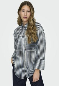 Camisa de botones a rayas en azul marino y blanco, con dos bolsillos en el pecho, mangas enrolladas y un corte holgado. Confeccionada en una tela ligera de textura suave.