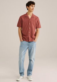 Korte mouw, rode, gestreepte overhemd met een camp collar, gecombineerd met lichtblauwe spijkerbroek en witte sneakers, met een relaxte pasvorm en knoopsluiting.
