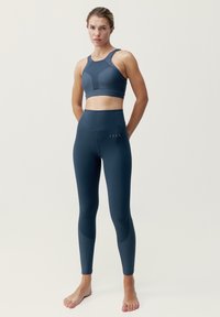 Námořnická modrá sportovní podprsenka a legíny s vysokým pasem, vyrobené z elastického materiálu, s panely a hladkou texturou.