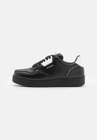 Sneaker nera con tomaia in pelle liscia, accenti bianchi, punta perforata, lacci piatti e suola in gomma nera spessa. Presenta il marchio di fabbrica sul lato.