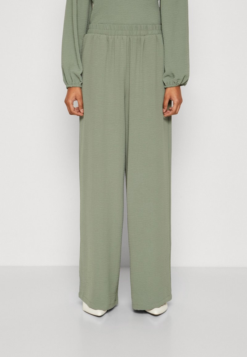 Pantalon ample vert clair en tissu texturé, avec une ceinture élastique et des poches latérales, offrant une coupe ample et confortable.