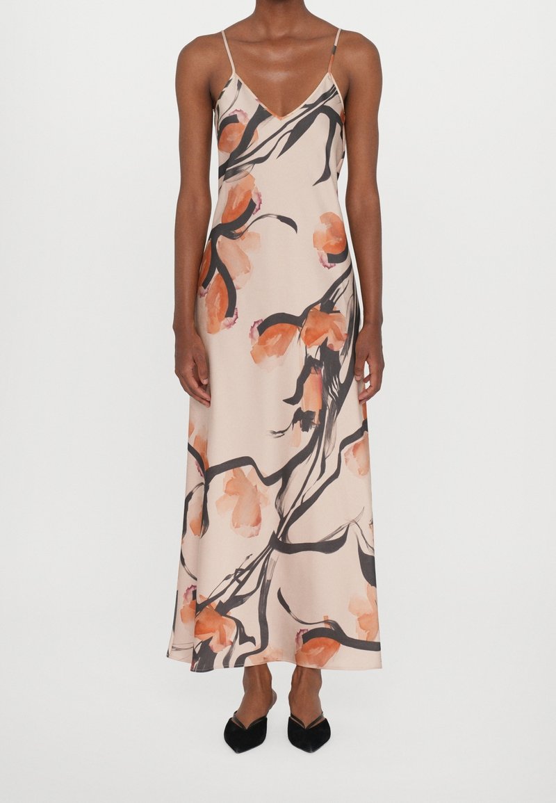 Robe maxi en satin à fleurs de couleur beige doux avec des fleurs orange et des branches noires. Elle présente des bretelles spaghetti fines et une silhouette fluide.