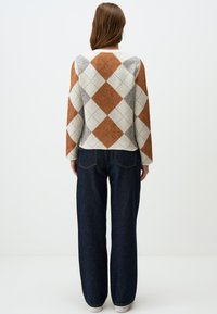 Pull en tricot avec un motif argyle orange, crème et gris ; manches larges ; associé à un jean en denim foncé taille haute ; texture lisse.