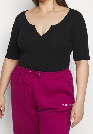Vrouw die een zwarte geribbelde top met V-hals, ellebooglange mouwen en een hooggetailleerde magenta sweatpants met trekkoord en "MISSGUIDED"-logo draagt.