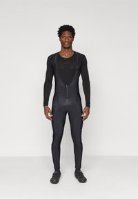 Čierny cyklistický dres s dlhými rukávmi, zapínaním na zips vpredu, vypchatým sedadlom a priliehajúcimi nohavicami. Hladká textúra a minimalistický dizajn. Čierne cyklistické topánky.