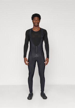 Čierny cyklistický dres s dlhými rukávmi, zapínaním na zips vpredu, vypchatým sedadlom a priliehajúcimi nohavicami. Hladká textúra a minimalistický dizajn. Čierne cyklistické topánky.