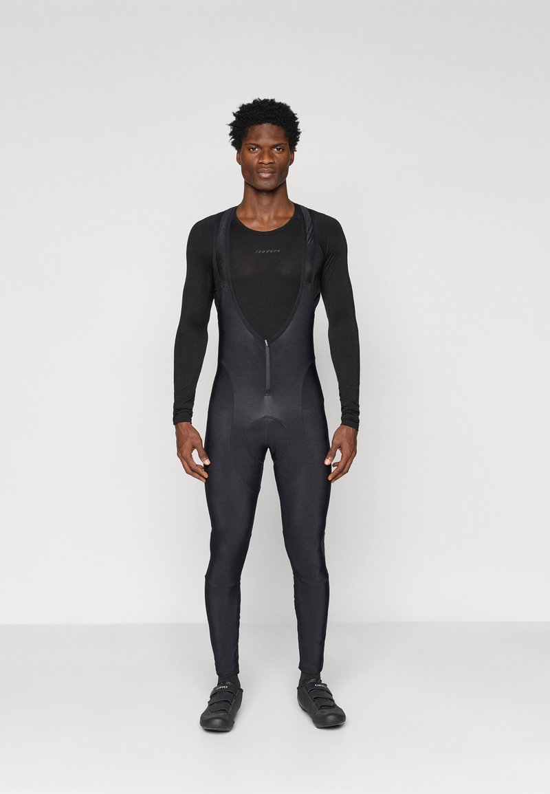 Čierny cyklistický dres s dlhými rukávmi, zapínaním na zips vpredu, vypchatým sedadlom a priliehajúcimi nohavicami. Hladká textúra a minimalistický dizajn. Čierne cyklistické topánky.