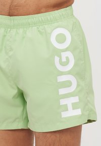 Svijetlozeleni kupaći šorts od glatkog materijala, s velikim bijelim logotipom "HUGO" s lijeve strane. Elastični pojas za udobnost.