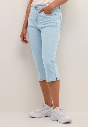 Pantaloni capri azzurri chiari a coste con un design aderente, due tasche laterali e uno spacco all'orlo, abbinati a sneaker bianche.