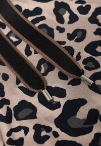 Tissu imprimé léopard en beige et bleu foncé, avec deux fermetures éclair noires munies de tirettes en tissu marron et embouts métalliques. Texture douce.