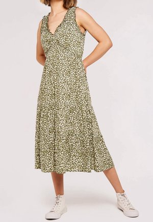 Oliwkowa sukienka bez rękawów z dekoltem w serek, falbankami, kwiatowym wzorem i warstwową spódnicą; noszona z białymi trampkami.