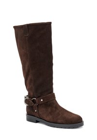 Bota alta de ante marrón con suela de goma plana, que presenta un puño ancho, correa en el tobillo y detalle de hardware circular.