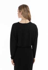 Schwarzes Langarmtop mit lässigem Schnitt, runder Ausschnitt und überschnittenen Schultern. Glatte Textur und minimalistisches Design.