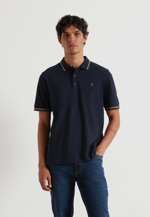Marineblauwe polo met korte mouwen, voorzien van een drieknoopssluiting, een witte en beige gestreepte kraag en een geborduurd logo op de borst.