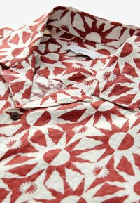 Kurzarmhemd mit rot-weißer Sonnenstrahlenmuster, Kentkragen und braunem Knopf aus Textil.