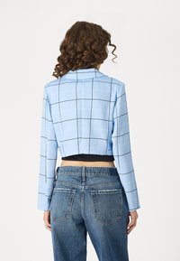 Kuttet blå blazer med rutemønster, med lange ermer og skreddersydd krage, kombinert med høy midje denimjeans.