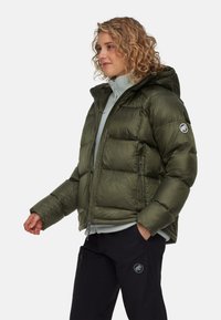 Olijfgroene pufferjack met capuchon, geborduurd ontwerp, rits aan de voorkant en zijzakken. Bevat een embleem op de linkermouw.