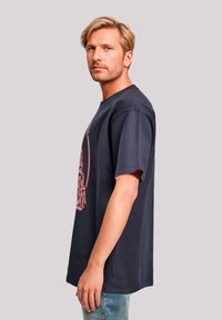 Navy cotton t-shirt featuring a large pink graphic design on the front, short sleeves, and a relaxed fit, paired with light denim jeans.
