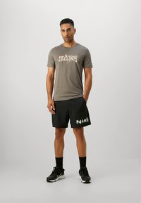 Grå bomulls-T-skjorte med stilisert "Nike"-logo; svarte shorts med hvit "Nike"-tekst; svarte treningssko; sokker synlige.