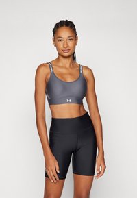 Sujetador deportivo gris con tirantes con logotipo, textura suave y un diseño ajustado, combinado con pantalones cortos de ciclismo negros de cintura alta.