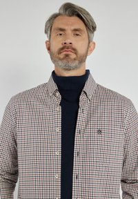 Koszula w kratę zapinana na guziki w kolorze czerwonym, granatowym i białym, zestawiona z granatowym golfem. Posiada kieszeń na piersi oraz klasyczny design kołnierza.