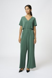 Mono verde con escote en V, mangas cortas y cintura elástica. Fabricado en una tela suave con perneras anchas. Combinado con tacones negros de punta.