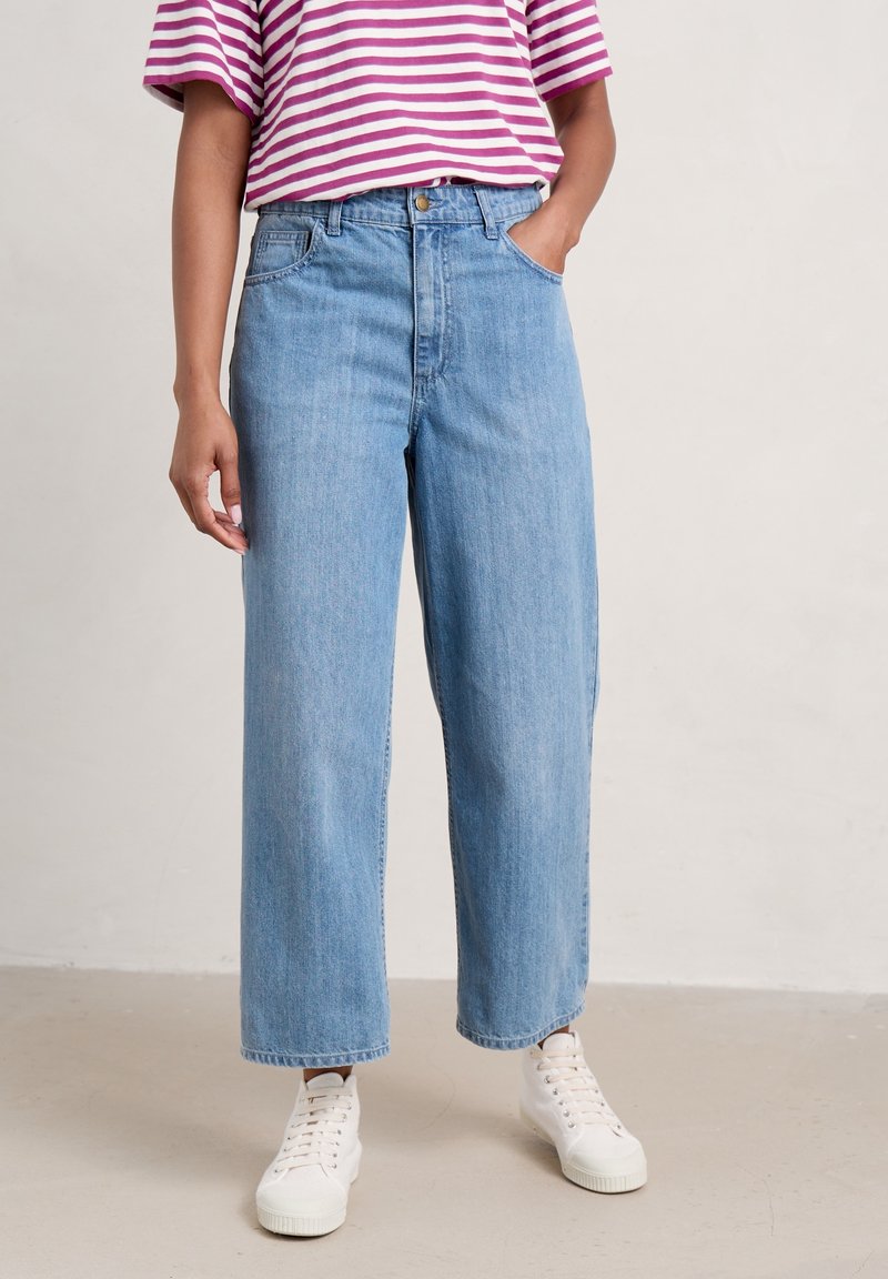 Light blue wide-leg jeans with a high waist, featuring front pockets and a subtle wash, paired with a pink and white striped oversized T-shirt.