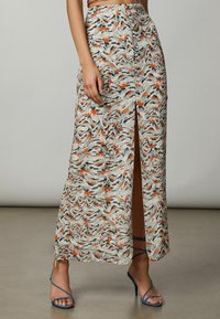 Falda larga de tela ligera con un patrón abstracto multicolor, abertura lateral y cinturilla ajustada. Combinada con tacones azules de tiras.