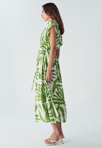 Maxi haljina u zelenom i bijelom uzorku lišća, izrađena od lagane tkanine. Ima kratke lepršave rukave i elastičnu urezanu struk.