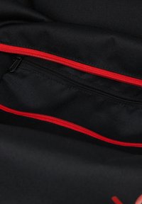 Interno di una borsa in tessuto nero con cerniere rosse visibili. Presenta una piccola tasca con cerniera e una superficie texturizzata, che offre organizzazione e spazio di archiviazione.