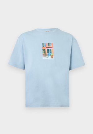 Hellblaues kurzärmeliges Hemd mit einer bunten Grafik einer Hausfassade, einem Fahrrad und einer Topfpflanze in der vorderen Mitte.