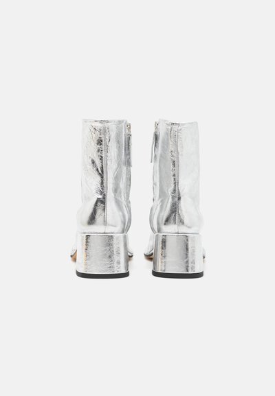 Botine din piele argintie, cu un finisaj texturat, închidere cu fermoar și toc metalic gros. Suprafață netedă și design elegant.