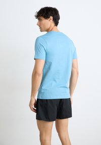 Lyseblå T-skjorte med kort erm laget av mykt stoff, kombinert med svarte shorts. Skjorten har en rund halslinning og en tettsittende silhuett.