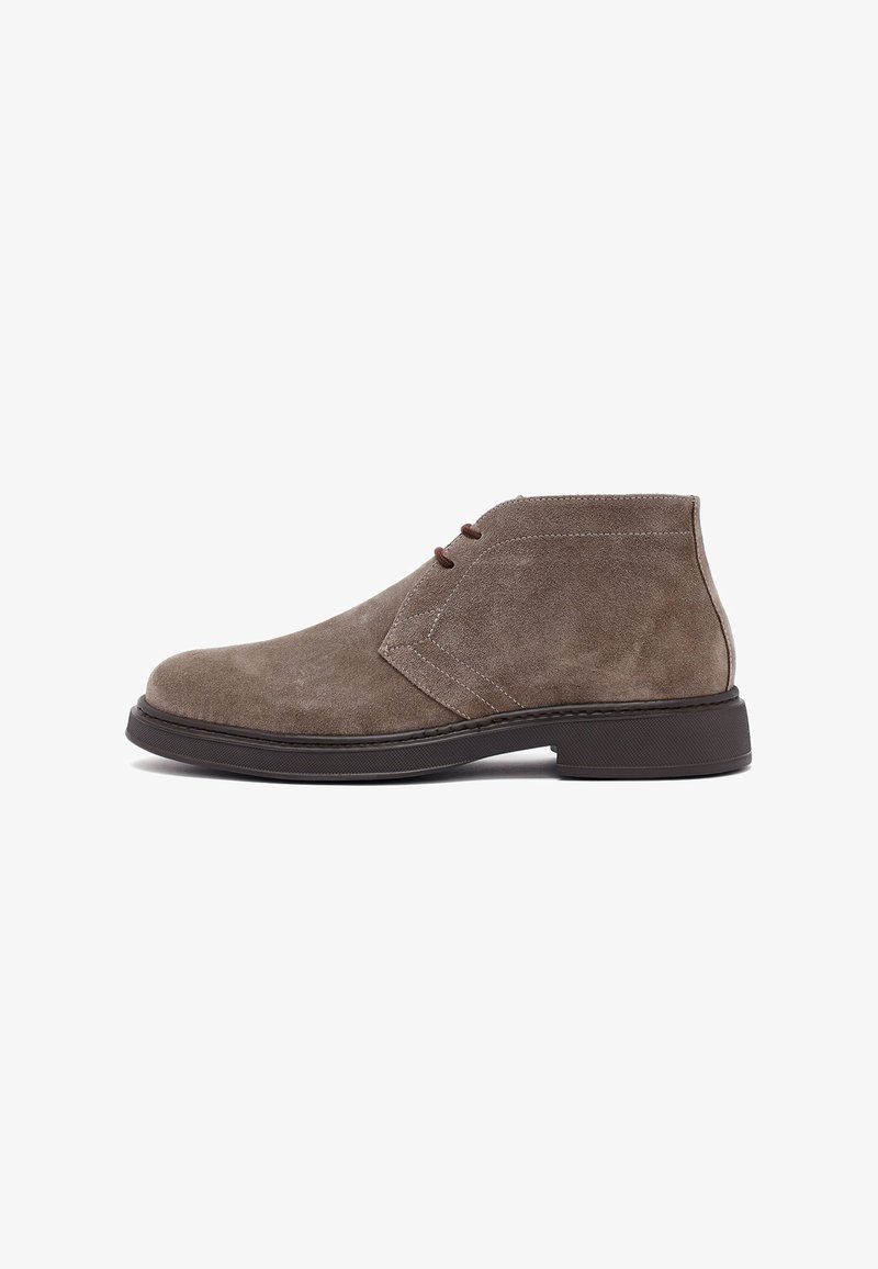 Heren taupe suède enkellaarzen met een donkerbruine rubberen zool en een vetersluiting met twee gaatjes, weergegeven vanaf de buitenkant.