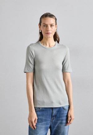 Tricou tricotat de culoare gri deschis, cu mâneci scurte, decolteu rotund și textură netedă. Asortat cu blugi din denim bleu.