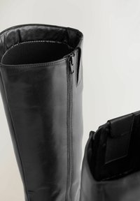 Czarne skórzane kozaki za kolano z bocznymi zamkami i wyściełanym wnętrzem, przedstawione z góry na jasnym tle.