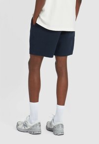 Marineblau Shorts aus strukturiertem Stoff mit Seitentaschen, kombiniert mit weißen Socken und grauen Sportschuhen, von hinten betrachtet.