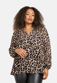 Blusa in stampa leopardata beige e nera, con chiusura a bottoni, maniche lunghe con polsini elasticizzati e vestibilità morbida.