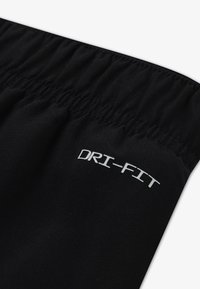 Cintura preta DRI-FIT com um design elástico e franzido. O material é suave com um leve brilho, realçando a sua aparência atlética.