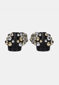 Zapatos negros con adornos metálicos en plata y oro, con una forma redondeada y una superficie texturizada. Presentan acentos de tachuelas decorativas.