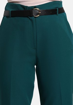 Teal high-waisted trousers with a front pleat, paired with a black leather belt featuring a circular gold buckle and subtle sheen.